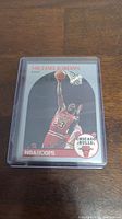 Front of Michael Jordan 1990 NBA Hoops basketball card in protective case, showing Jordan dunking in Bulls jersey.