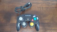 Front view of black Nintendo GameCube controller showing control stick, directional pad, main buttons, and cable.