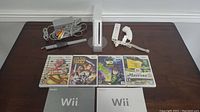 White Nintendo Wii console standing vertically with sensor bar, power supply, AV cables, Wii Remote, Nunchuk, and four games displayed on table.