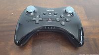 Top front view showing button layout, analog sticks, and power button on glossy black surface.