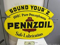 Oval yellow Pennzoil metal sign with black text and red logo