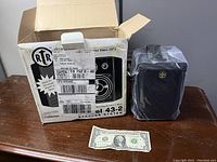 Photograph showing an RTR Model 43-2 stereo speaker system box next to one wrapped speaker and a one dollar bill for scale.