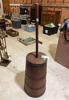 Full view of wood butter churn standing upright showing cylindrical barrel base and long dasher handle.