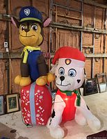Front view of Chase and Marshall Paw Patrol Christmas inflatables illuminated and inflated, sitting on a large wrapped Christmas present
