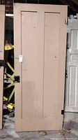 Full frontal view of beige painted solid wood door with two vertical panels and attached hardware.