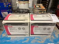 Two new Sure-Lites emergency auxiliary lighting units in original boxes on a table with packaging text and graphics visible.