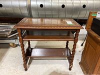 Front view of wooden end table showing tabletop with carved border and two shelves below supported by spiral and turned legs.