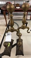 Pair of brass andirons with large round finials and cast iron bases on a reflective surface, showing the entire pair.