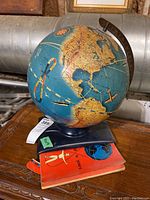 Globe and book together showing size and colors, on wooden surface.