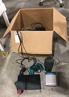 Box containing the PlayStation 2 console, blue wired controller, Dell speaker, networking router, and various cables.