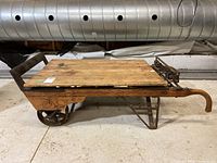 Side view of wooden platform scale showing spoked wheel, fold-out legs and handles