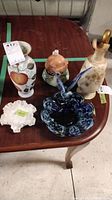 Photo showing the full set of Doulton Burslem pieces including pitcher, vase, lidded teapot, cream ruffled bowl, and blue glass bowl on a wooden table.