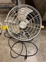 Front view of Canarm metal wall fan showing protective white cage, fan blades, power cord with plug.
