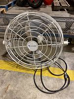 Front view of white Canarm metal wall fan showing protective grill and fan blades.