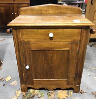 Front view showing drawer, paneled cabinet door with white knobs, and front scalloped base edge.