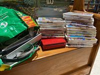 Photo of red Nintendo Wii console and 5 Wii game cases stacked beside it along with accessories in a bag.