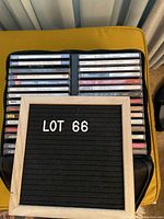 Photo showing approximately 34 CDs arranged in two rows inside a black CD carrying case on a yellow background, accompanied by a letter board labeled 'LOT 66'.