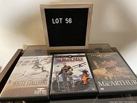 Photo of three DVD cases: Legendary White Stallions, The Blue Max, and MacArthur with a letter board reading LOT 56.