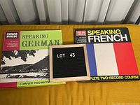 Two boxed sets of language learning albums displayed side by side; one Speaking German, one Speaking French, with a lots marker in the middle
