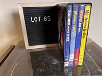 Photo showing four Miss Marple DVDs standing upright next to a sign with lot number 65.