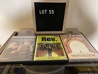 Three DVD cases displayed on a turntable with a sign reading LOT 55. Titles visible: Grantchester Season 2, Rev Season 1, Monsignor movie.