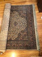 Partially rolled area rug showing overall pattern and fringe.