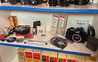 Overview of entire lot on shelf showing both cameras, flash unit, filters, cables and accessories