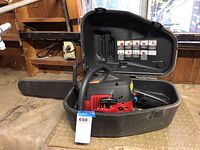 Chainsaw inside open carrying case on workbench, showing overall size and condition