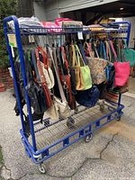 Front side view of the blue metal rolling rack with various bags hung on hooks and placed on the shelves.