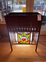 Front view of wood plant stand with stained glass insert visible in lower front panel, showing colorful floral and dragonfly pattern.