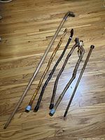 Six wooden walking sticks laid on floor showing variety of handles and wood tones, including carved dragon head staff