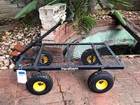Angle view of YardSam garden cart dolly showing mesh platform surface and yellow-rimmed pneumatic tires on brick patio.