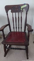 Front view of the child's wooden rocking chair showing detailed carved backrest and leather seat.