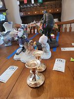 Photo showing Precious Moments figurine, Lenox Christmas scene figurines, signed golfer statue, and two silver-toned candle holders on wooden table.