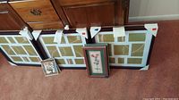 Photo showing all three multi-photo frames in dark wood finish and four smaller framed artworks arranged on carpeted floor
