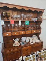 Wooden kitchen hutch with glassware on top shelves and ceramic dishware on lower countertop