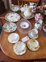Overview of bone china and porcelain items on wooden table including pitchers, plates, trinket dish, and multiple teacups and saucers
