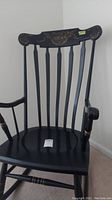 Front view of black wooden rocking chair with vertical slats and fruit design on top backrest