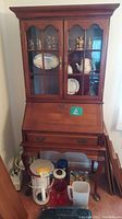 Front view showing the closed secretary desk, with 2 glass doors displaying dishes and collectibles inside. The 4 drawers below the drop-front desk surface are visible.