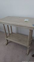 Full side view of the rectangular painted wooden table showing spindle legs and lower shelf, placed on carpeted floor.