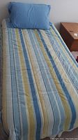 Twin bed made with striped comforter and blue pillow on top.