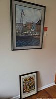 Photo showing the two framed artworks, one leaning against the wall, the other hanging: 'NOVEMBER' print with still life objects and boat print above