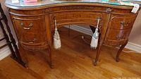 Front view of vanity table showing kidney-shaped glass top and drawer tassels