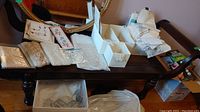 Table with multiple piles of lace doilies, placemats, and embroidered napkins in various colors and styles.
