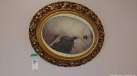 Oval vintage framed art print hanging on a wall, detailed view of frame and full artwork.