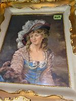Close-up of woman in feathered hat print framed in ornate gold frame with measurement sticker 20x18