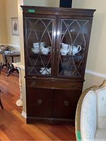 Full view of the wooden corner china cabinet showing the upper glass display area with geometric wood overlay and lower storage cabinet with drawer.