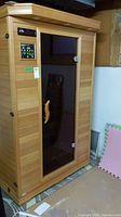 Exterior front view of sauna showing cedar panels, glass door, handle and stereo/control modules