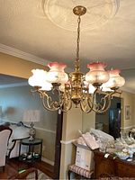 Full view of the chandelier hanging in a room, showing six frosted glass globes with pink ruffled rims and brass arms.