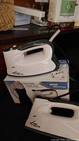 Two white Euro Steam Evolution steam irons shown resting on a box with product images and branding, featuring control knobs and handles.
